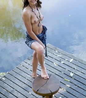 Раздетая молодая девушка сидит у воды